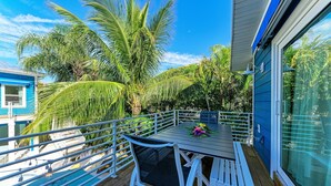 A balcony with a table and chairs, surrounded by lush greenery and a clear blue sky. - Blue Hideaway- 5 bedroom with Separate Guest House, Private Pool/Spa! (Anna Maria)