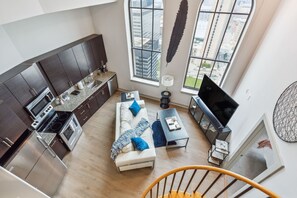 A modern kitchen with dark cabinets, a white sofa with blue cushions, and a large window offering a city view. - Distinguished Apartment Rooftop Deck (Baltimore)