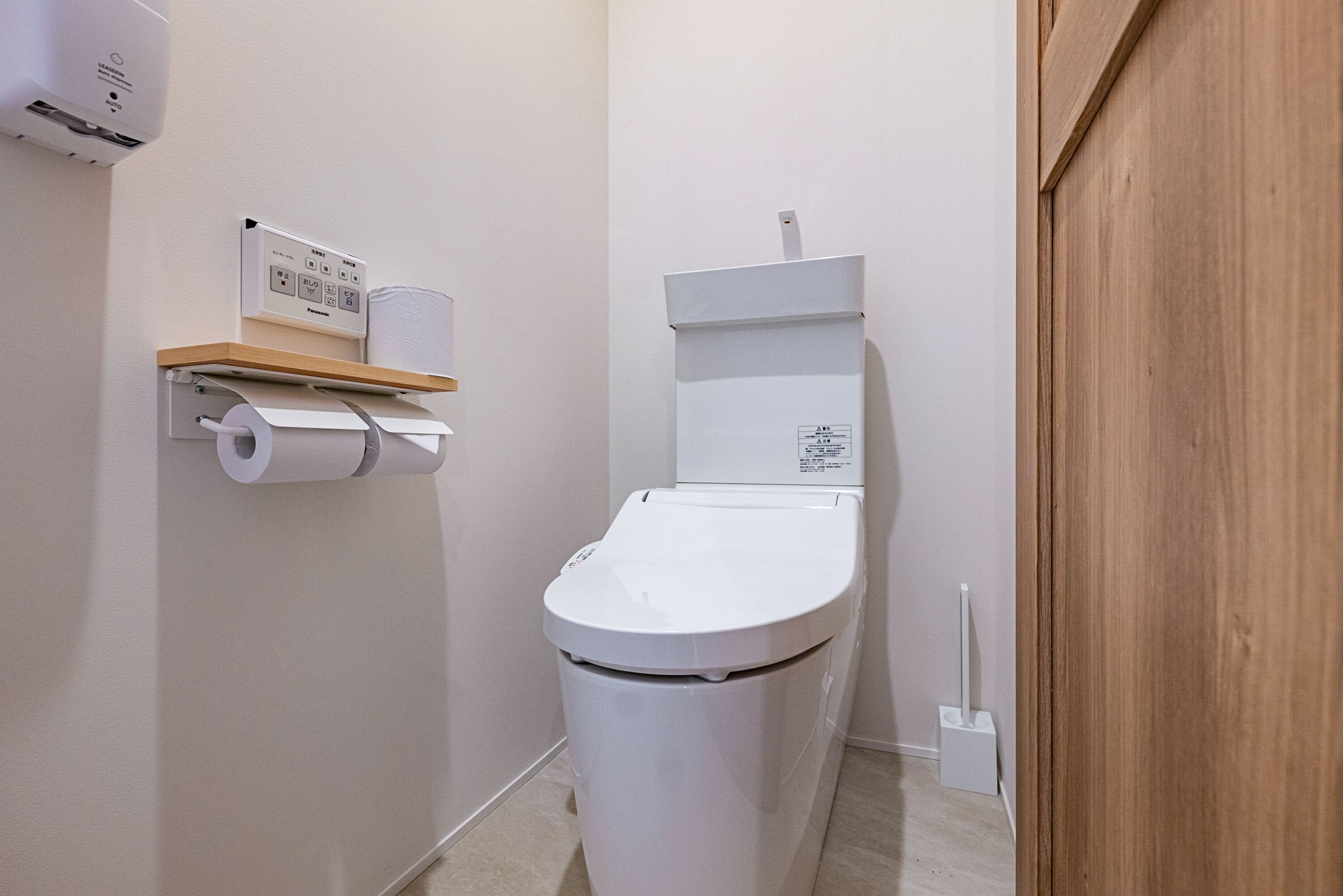 A small, modern bathroom with a toilet, a toilet paper holder, and a hand dryer.