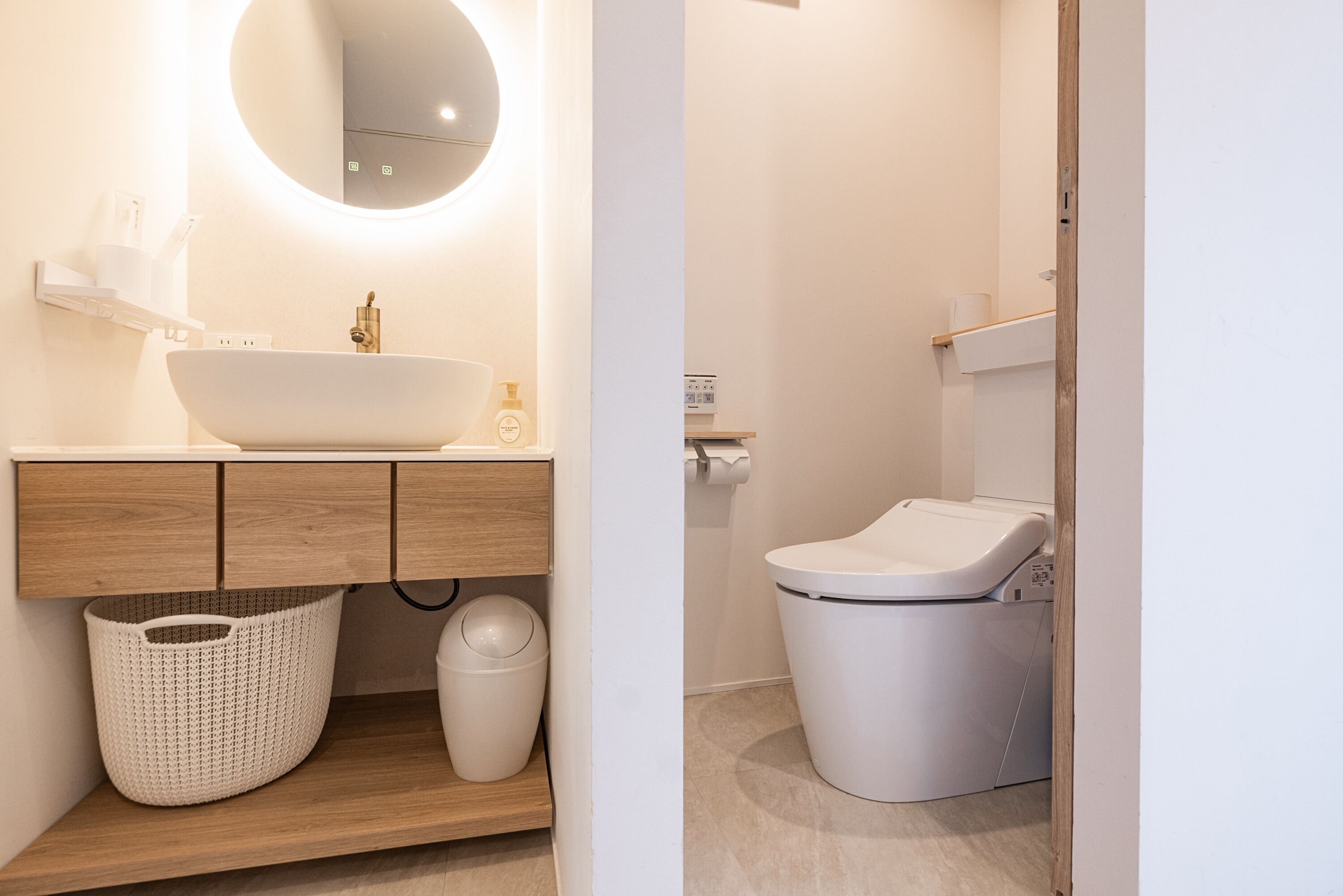 A modern bathroom with a large oval sink, wooden vanity, a round mirror, a white toilet, and a laundry area.