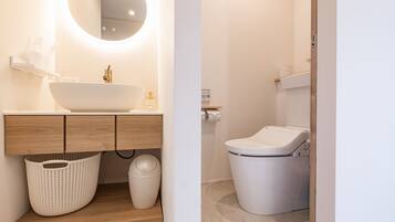 A modern bathroom with a large oval sink, wooden vanity, a round mirror, a white toilet, and a laundry area.