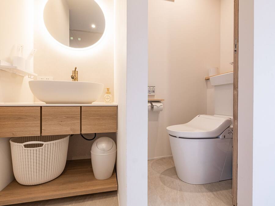A modern bathroom with a large oval sink, wooden vanity, a round mirror, a white toilet, and a laundry area.