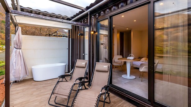 A modern outdoor area with a glass-enclosed room, a bathtub, and lounge chairs. - R MOGAMI (Tozawa)