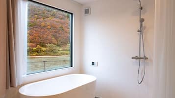 A bathroom with a bathtub, a shower, and a window with a view of autumn foliage.