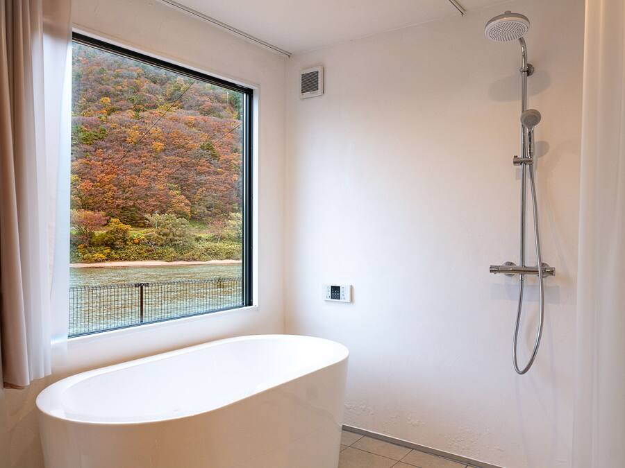 A bathroom with a bathtub, a shower, and a window with a view of autumn foliage.