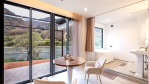 A modern room with a large window, a round table, two chairs, and a bathtub. - R MOGAMI (Tozawa)