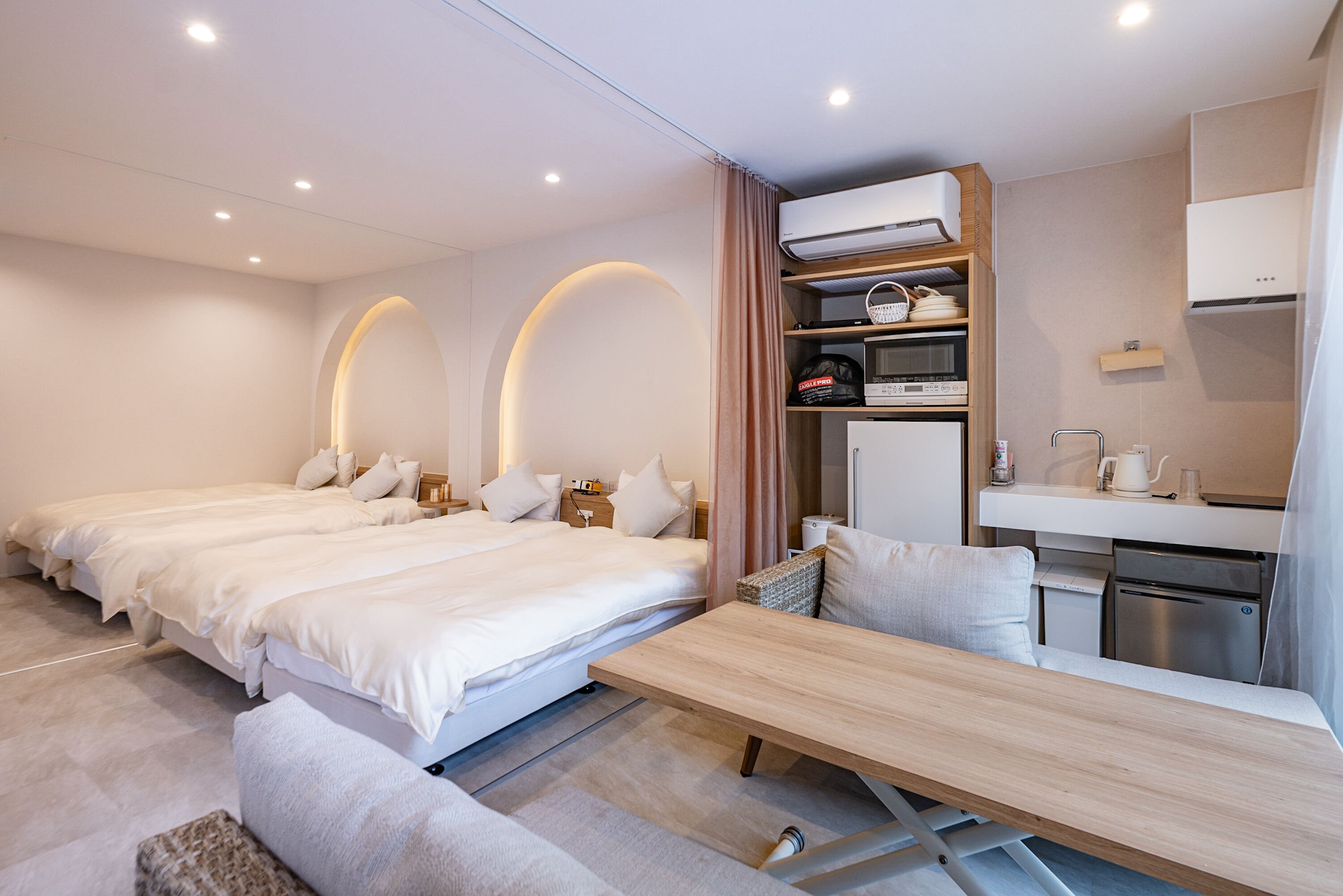 Ein modernes Hotelzimmer mit zwei Betten, einem Holztisch, einer Küchenzeile und einem integrierten Kleiderschrank.