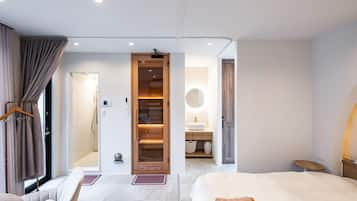 A modern hotel room with a bed, a seating area, a wooden wardrobe, and a bathroom visible through an open door.