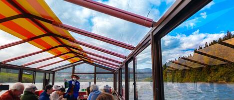 A boat with a covered deck, passengers seated, and a scenic river view.