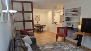 Un salon avec un canapé en cuir foncé, un fauteuil rouge, un pouf rond, une bibliothèque et un téléviseur.