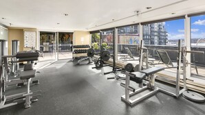 Une salle de sport équipée de divers appareils d’exercice, dotée de grandes fenêtres et offrant une vue sur les bâtiments.