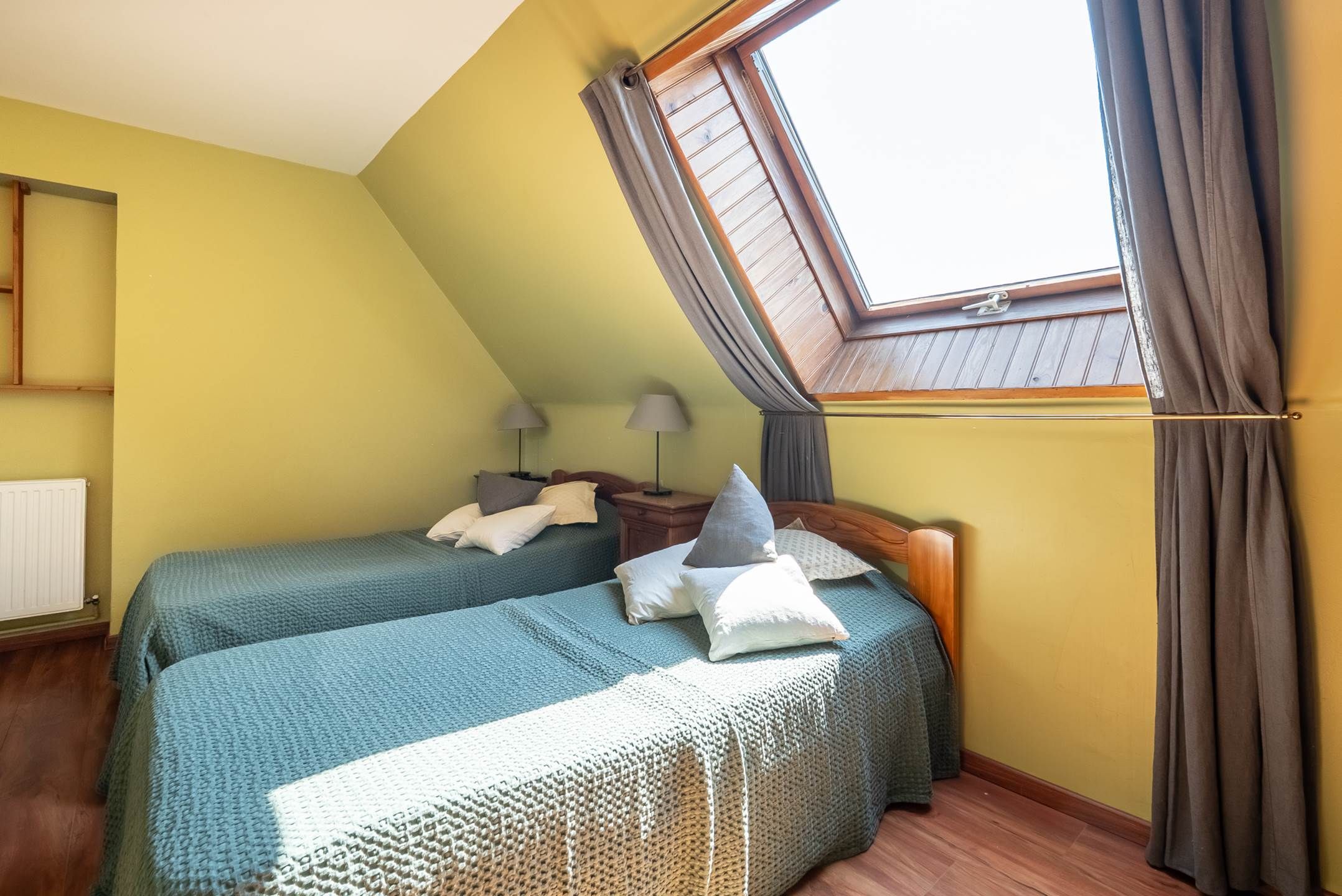 Une chambre avec deux lits, un puits de lumière, un radiateur et un plancher en bois.