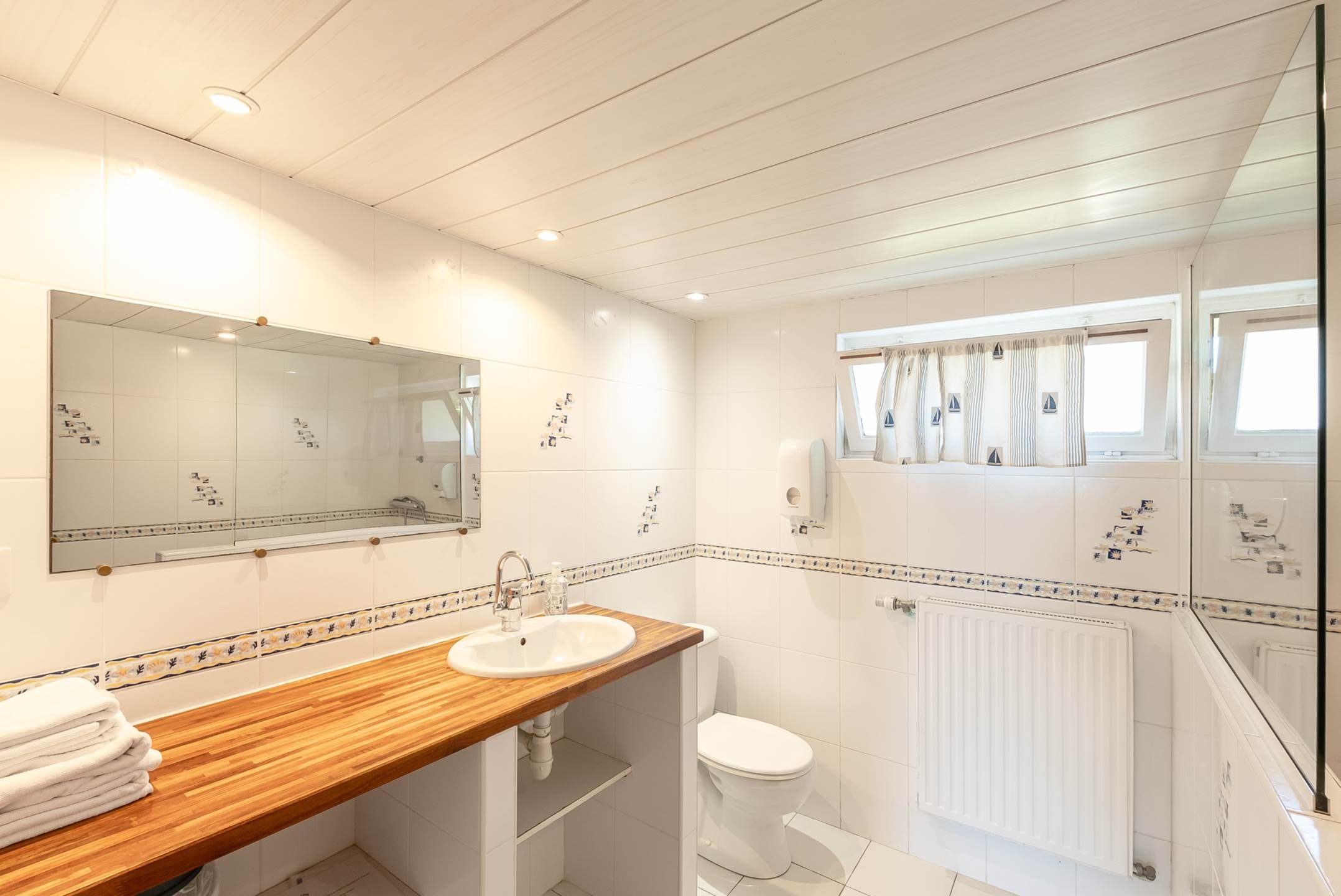 Une salle de bain avec un meuble-lavabo en bois, un lavabo, des toilettes et un espace douche.