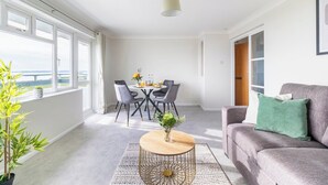 Un salon moderne avec un canapé gris, une table basse ronde et un coin repas comprenant une table et des chaises.
