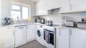 Une cuisine moderne avec des meubles blancs, un lave-vaisselle, une machine à laver, un four à micro-ondes et un grille-pain.