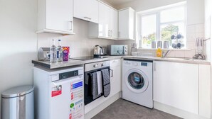 A modern kitchen with white cabinets, a dishwasher, a washing machine, and a window with a view of trees. - Beautiful Sea View 2 bedroom Sleeps 6-Free Parking (Bournemouth)