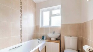 Un baño con bañera, lavamanos, inodoro y ventana.