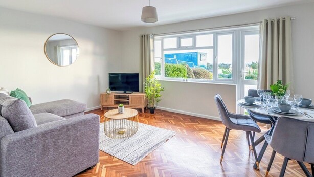 Una sala de estar moderna con un sofá, televisor, mesa de comedor y ventanas amplias.