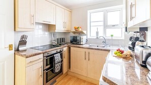 A modern kitchen with light wooden cabinets, a granite countertop, a built-in oven, a microwave, and a sink.