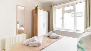A hotel room with a bed, a wooden wardrobe, a mirror, and a window with curtains.