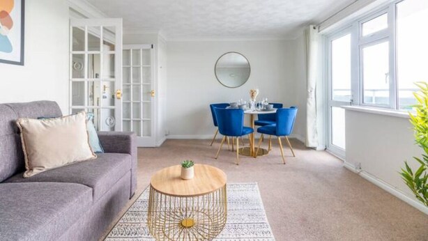 Un salon moderne avec un canapé gris, une table basse ronde et un coin repas comprenant des chaises bleues et une table blanche.