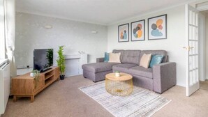 Un salon avec un canapé gris, une table basse ronde et un téléviseur posé sur un meuble en bois.
