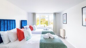 Une chambre d’hôtel avec deux lits, une grande fenêtre avec des rideaux, un radiateur et un tableau encadré au mur.