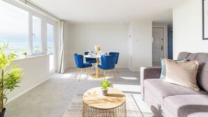 Un salon moderne avec un canapé gris, une table basse ronde et un coin repas comprenant des chaises bleues et une table blanche.
