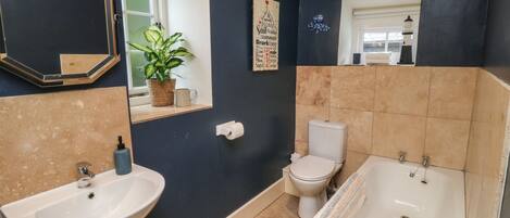 Une salle de bain avec un lavabo, des toilettes et une baignoire, une plante en pot et un miroir avec éclairage.