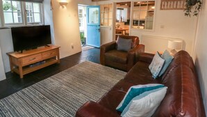 Un salon avec un meuble TV en bois, un canapé en cuir marron et un tapis à motifs.