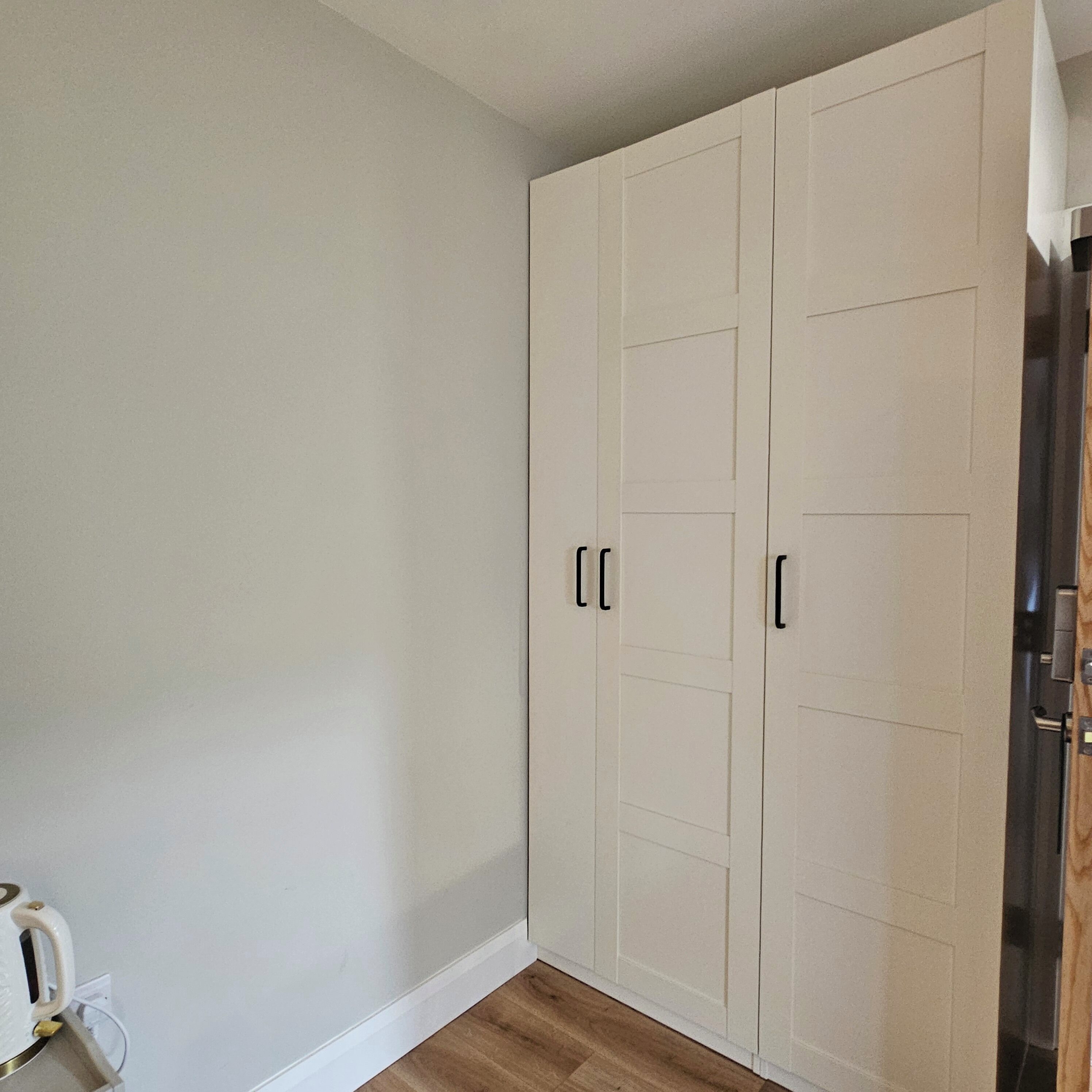 A room with a large white wardrobe, a wooden floor, and a white wall.