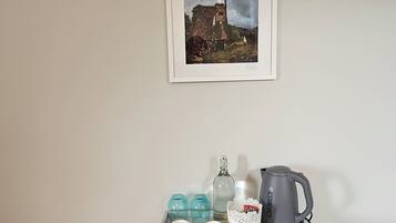 A white tray with a teapot, cups, and a bottle on a wall-mounted shelf.