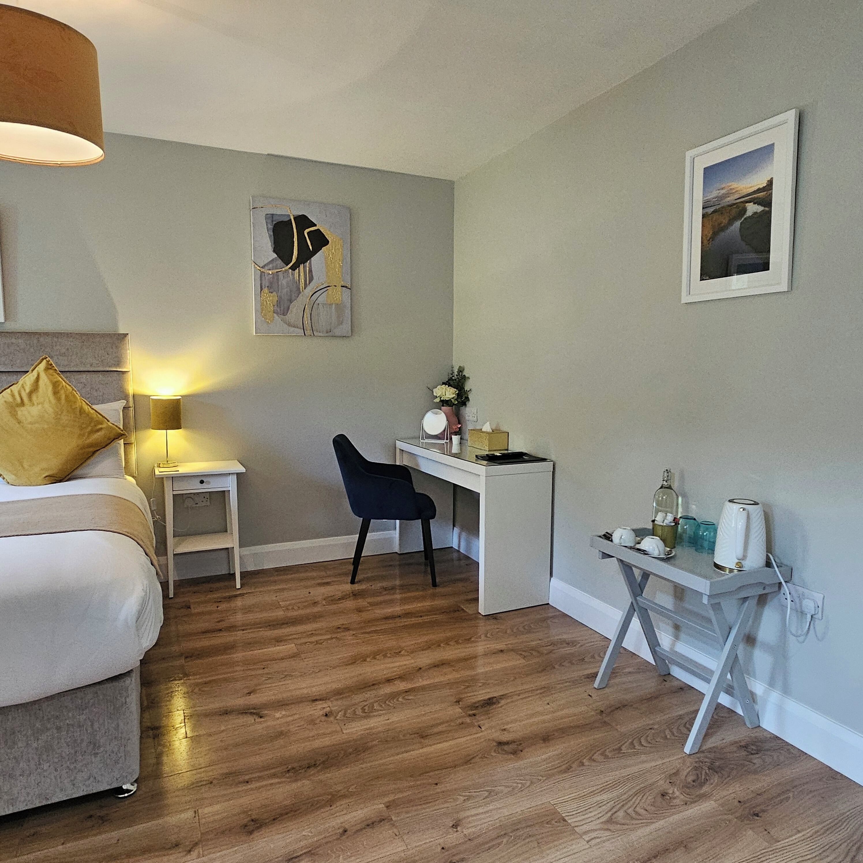 A bedroom with a bed, a desk, a chair, a nightstand, and a bedside table.