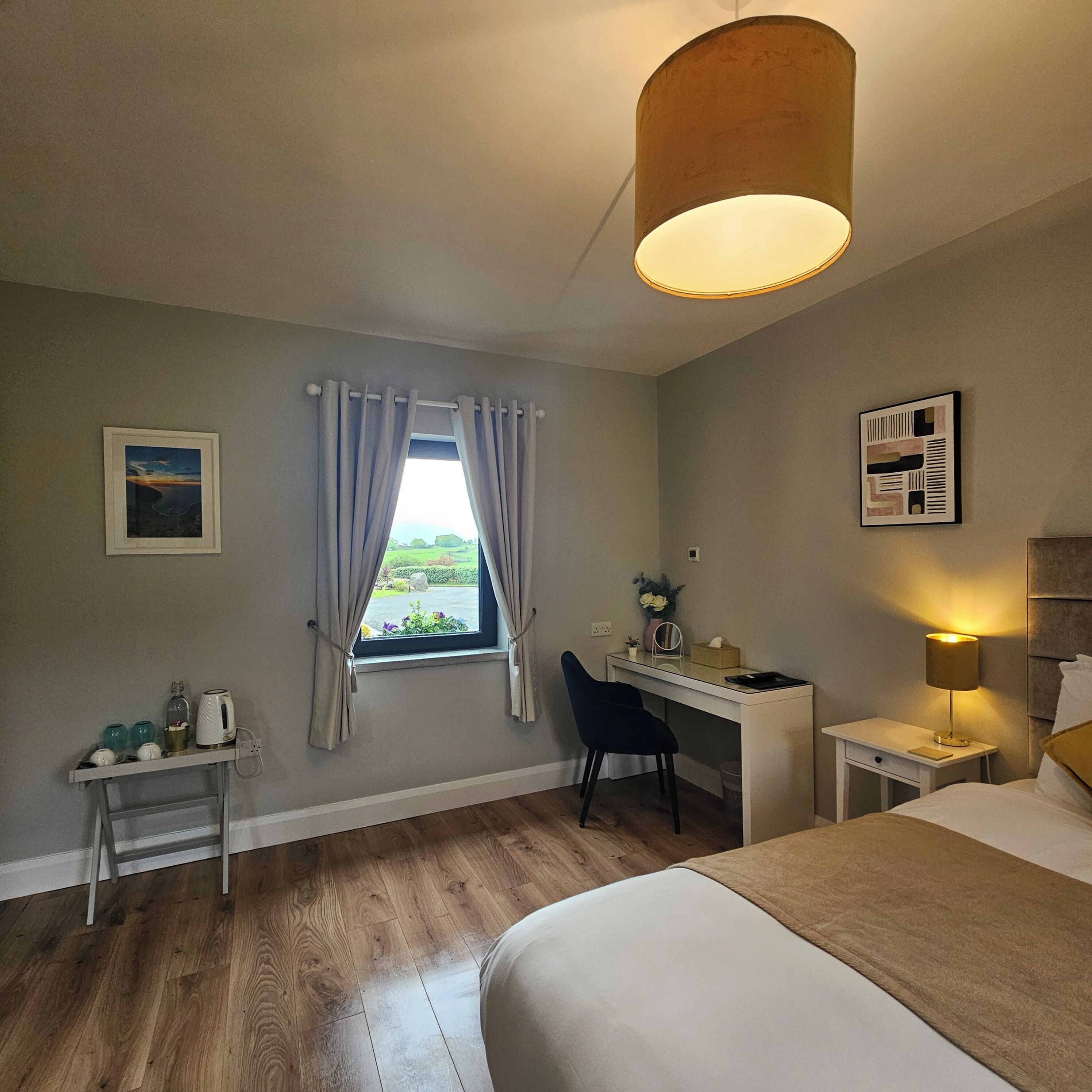 Habitación de hotel con cama, escritorio, silla, lámpara y ventana con cortinas.