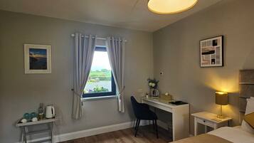 Habitación de hotel con cama, escritorio, silla, lámpara y ventana con cortinas.