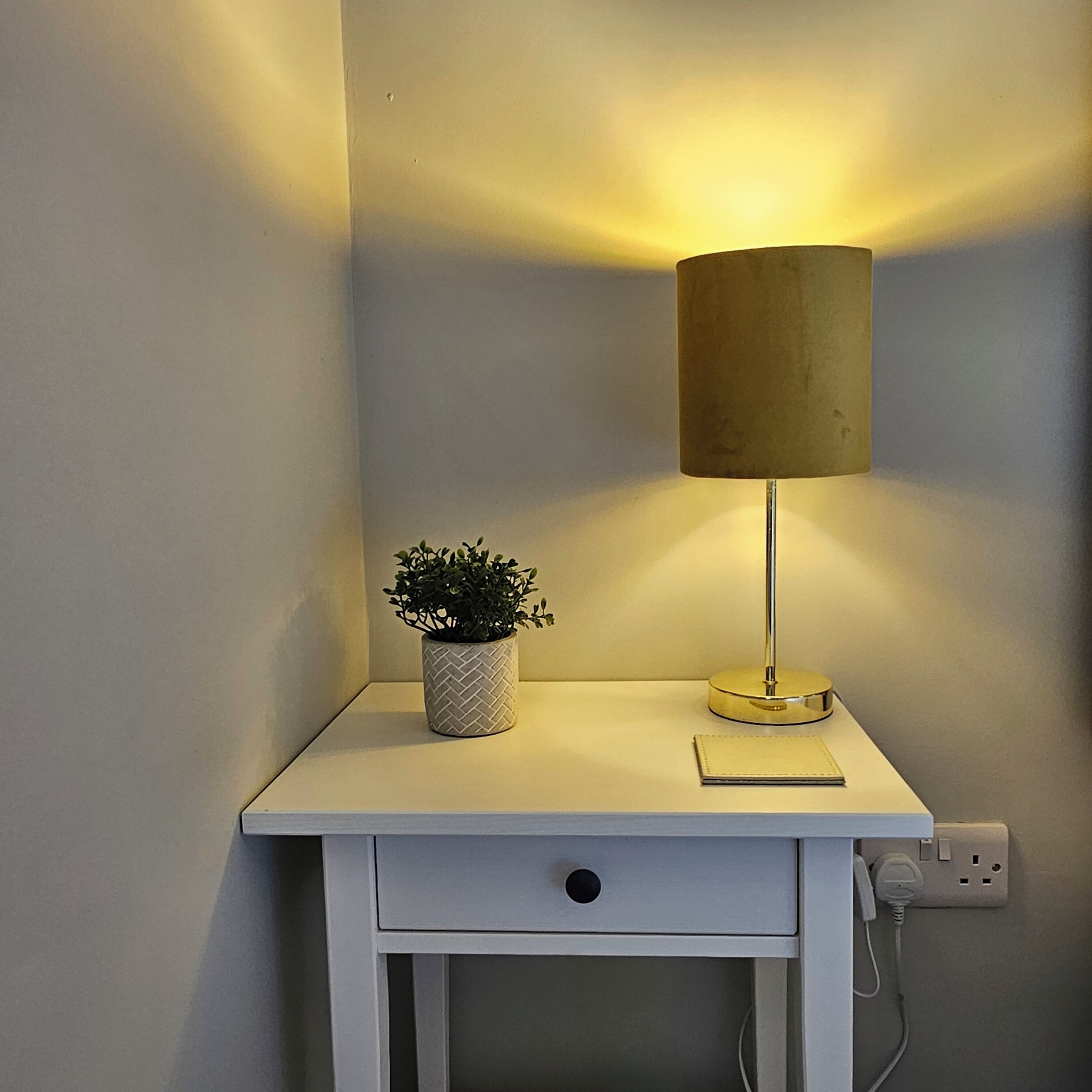 Een nachtkastje met een lamp, een kleine potplant en een stopcontact.