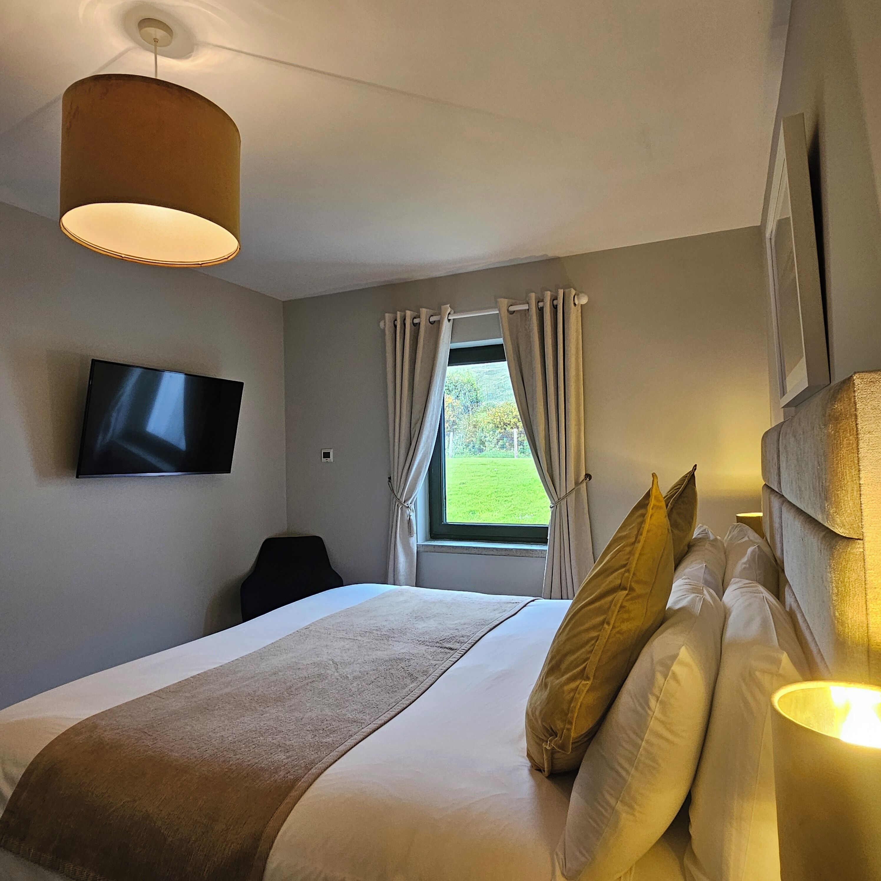 A hotel room with a bed, a TV mounted on the wall, a window with curtains, and a ceiling light.