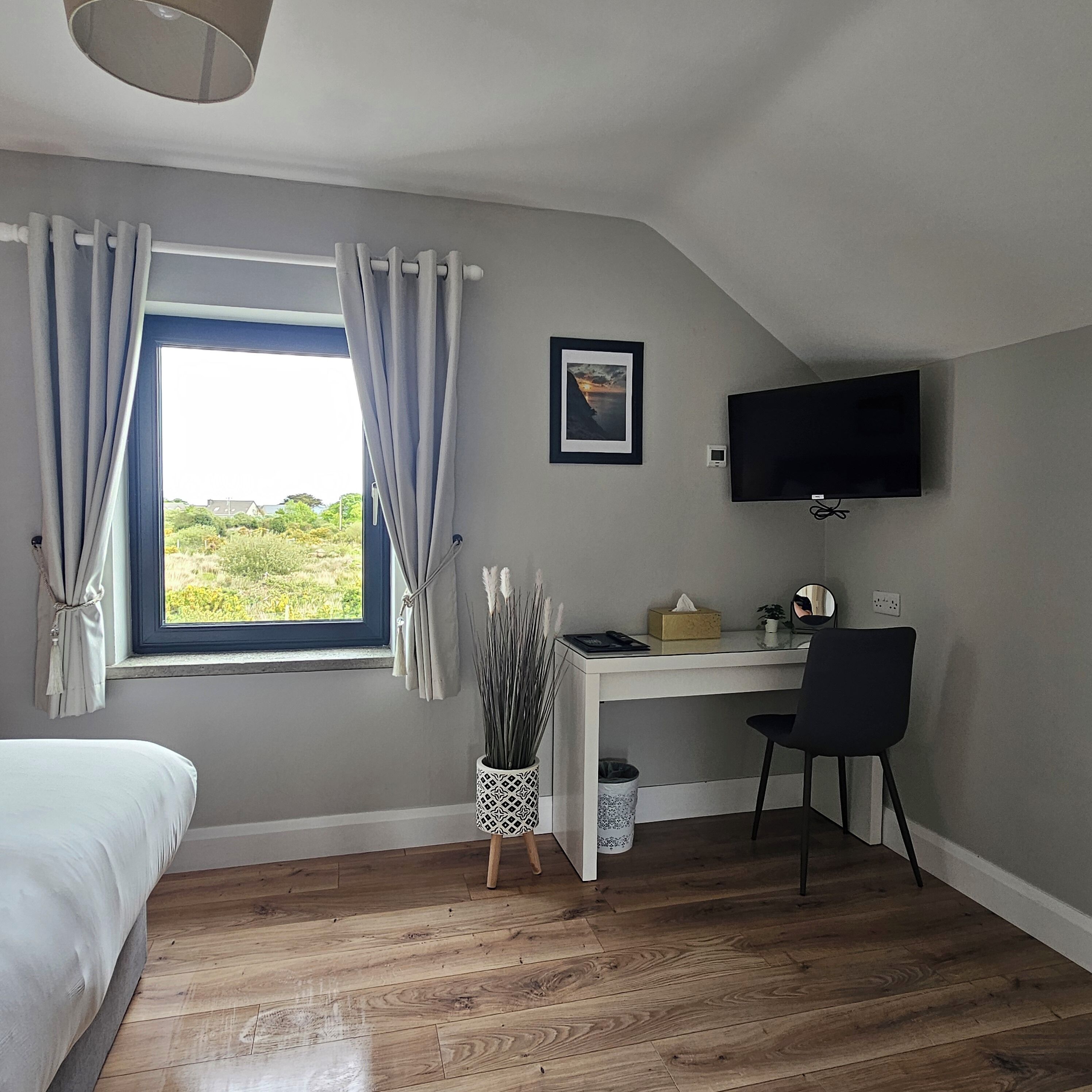 Un dormitorio con cama, escritorio, silla, televisor y ventana con cortinas.