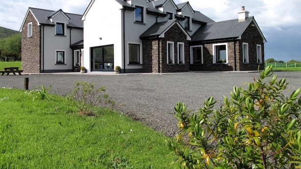 A modern two-story house with a stone facade, large windows, and a gravel driveway.