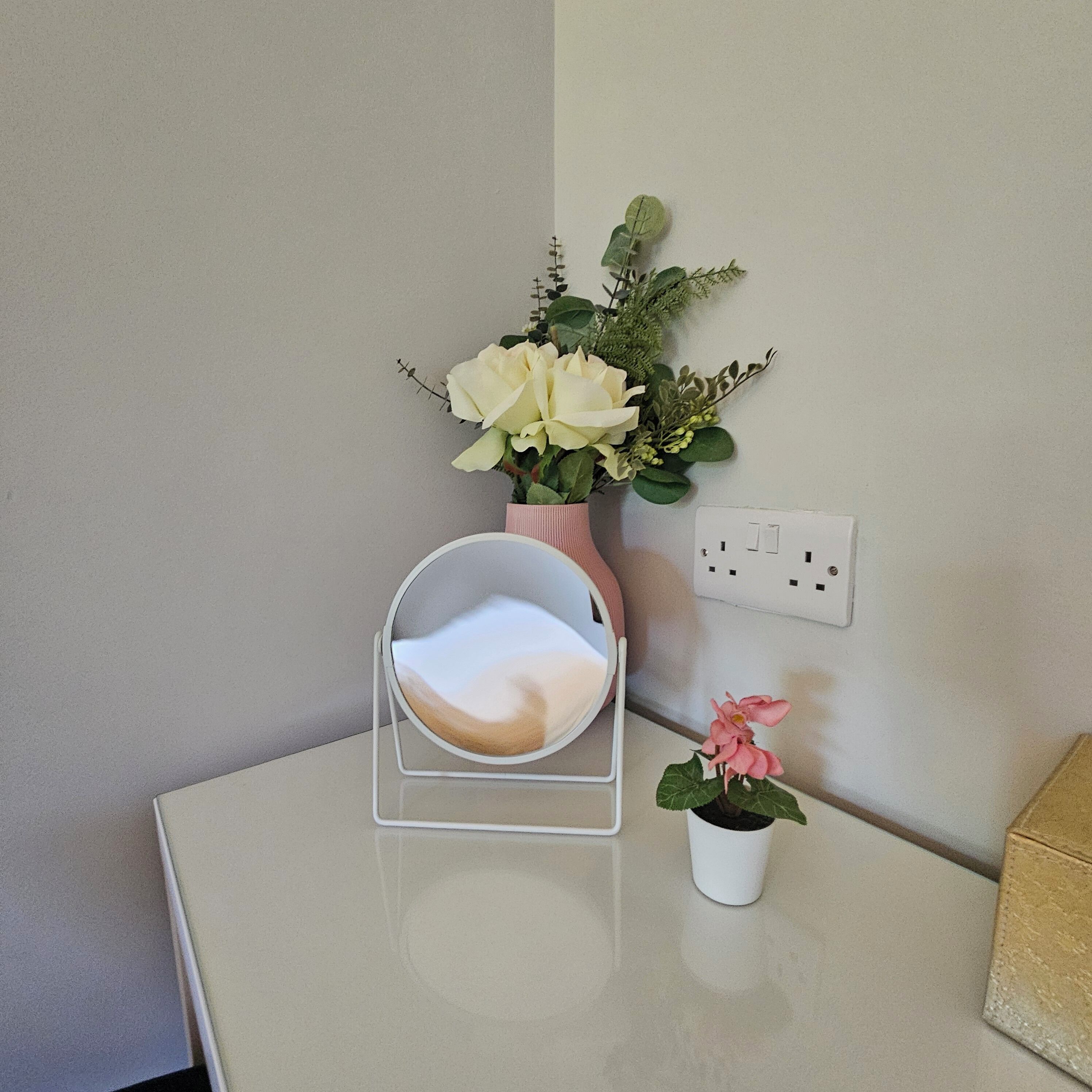 Une petite table sur laquelle se trouve un plateau blanc, un vase rose contenant des fleurs blanches et une petite plante en pot.