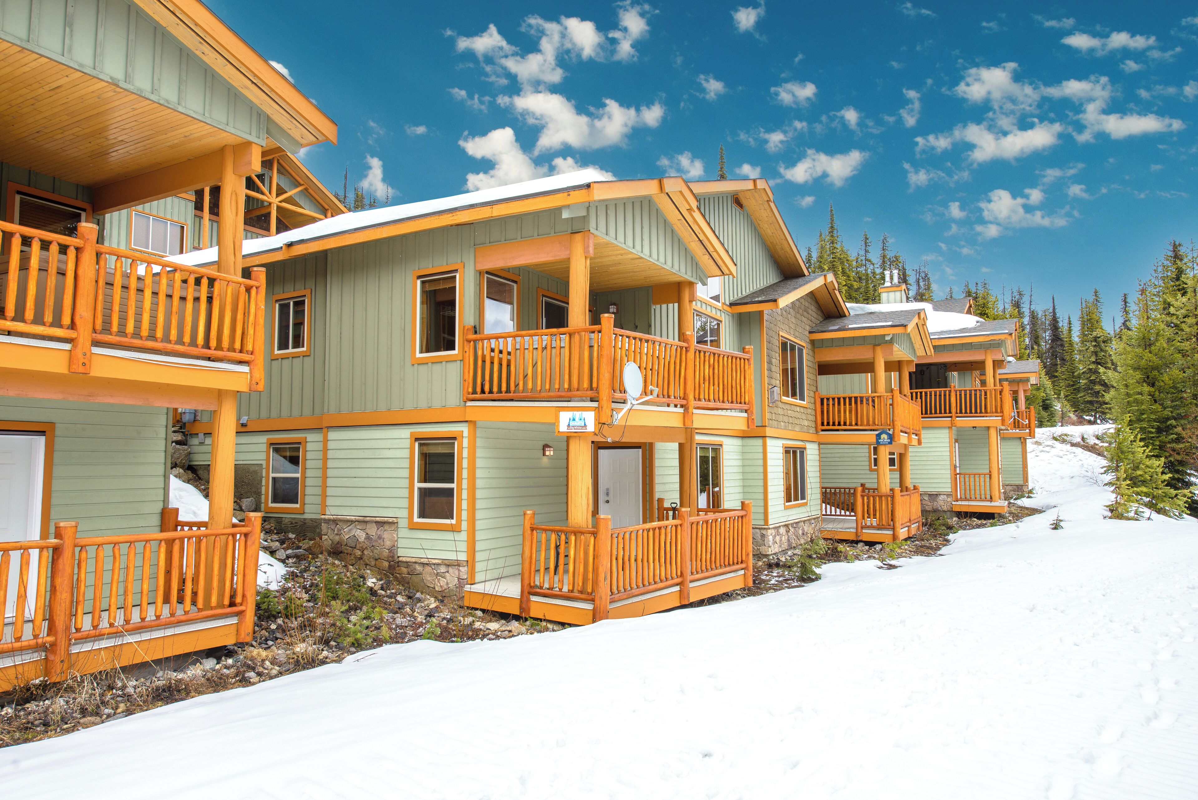 A row of log cabin-style buildings with wooden balconies and a snowy landscape.