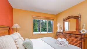 Ein Schlafzimmer mit Bett, Kommode, Spiegel und einem Fenster mit Blick auf Bäume.