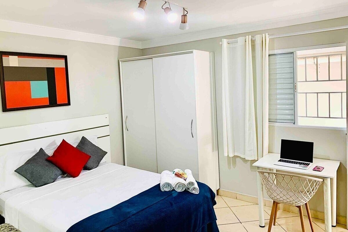 A hotel room with a bed, a desk with a laptop, a wardrobe, and a window with curtains.