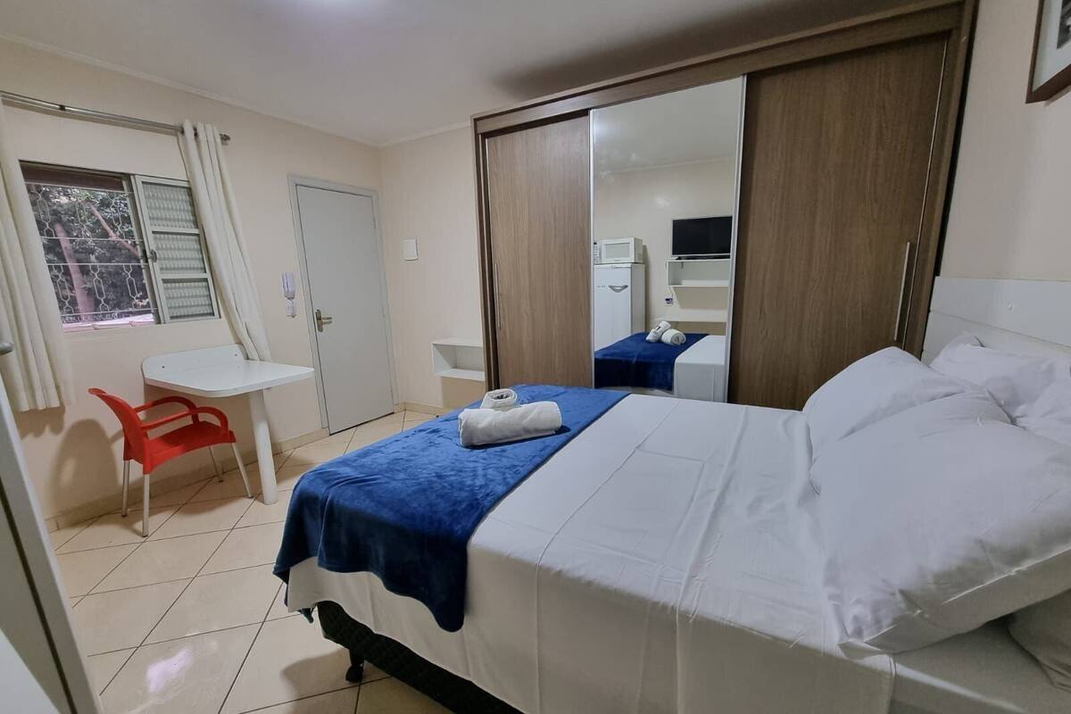 A hotel room with a bed, a desk, a chair, a wardrobe, and a window with curtains.