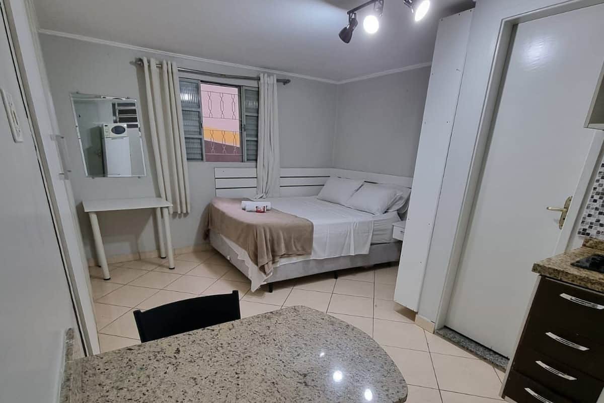 A compact bedroom with a bed, bedside table, and a small desk with a chair.