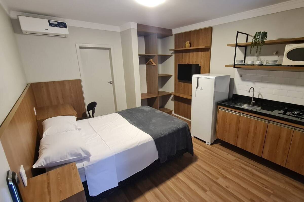 A compact room with a bed, a kitchenette, and a small seating area.