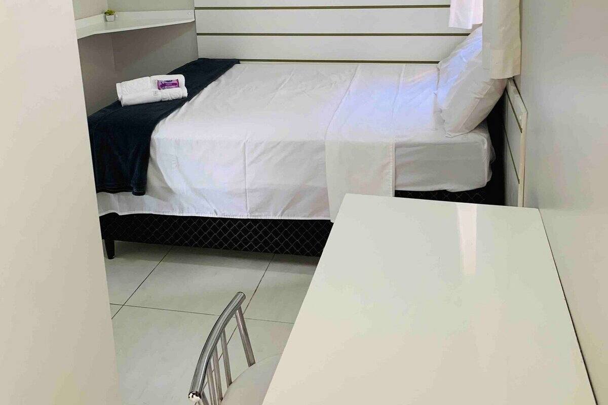 A small, single-bed room with a white bed, a small table, and a chair.