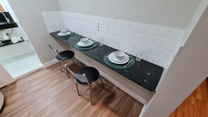 Eine Küche mit schwarzem Arbeitsplatz, weiß gefliestem Rückspritzschutz und drei Barhocker.