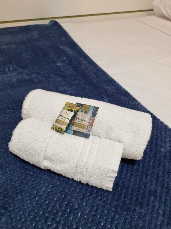 Tapete de banho azul com textura, um toalha branca dobrada e dois shampoos sólidos sobre ele.