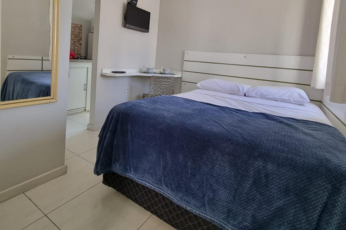 A bedroom with a bed, a TV mounted on the wall, and a bathroom visible through an open door.